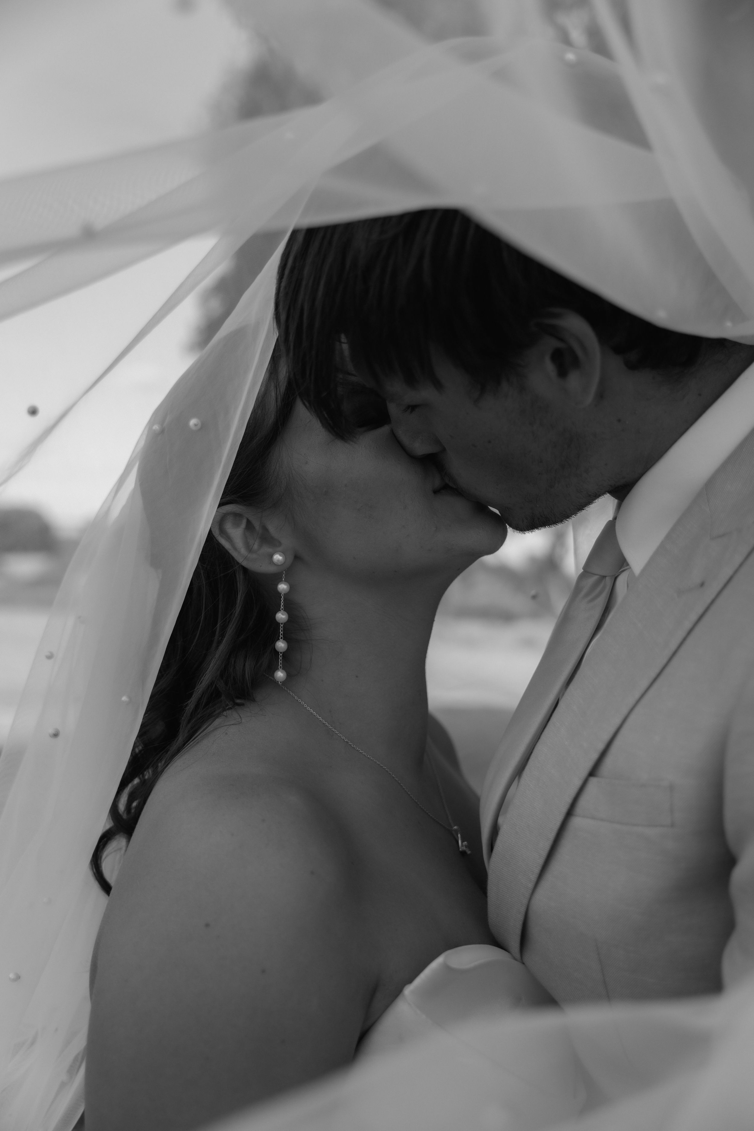 Black and white intimate portrait of couple sharing romantic moment under wedding veil.