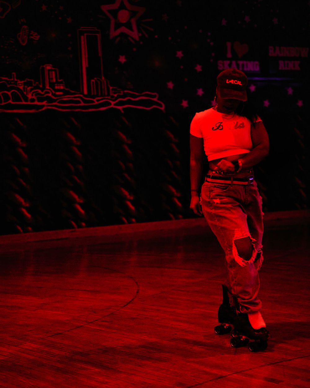 Silhouetted roller skater performs under dramatic red lighting on indoor rink.