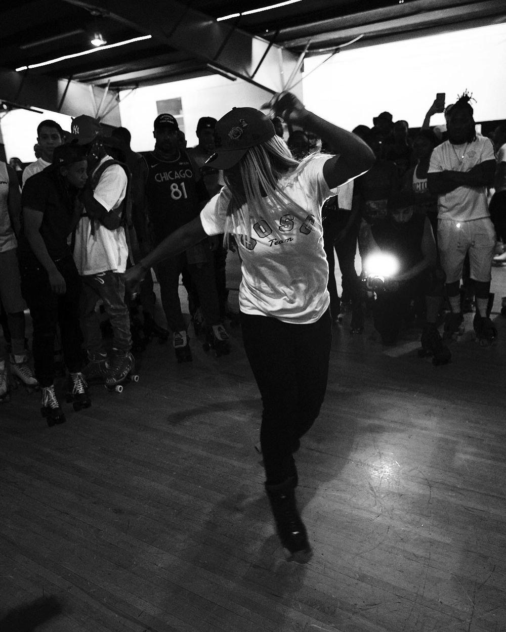 Person roller skating among crowd during indoor skating event captured in black and white.