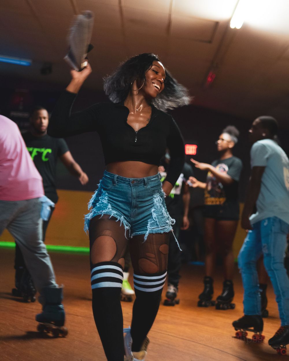 Energetic roller skater in crop top and denim shorts dances at indoor skating rink.