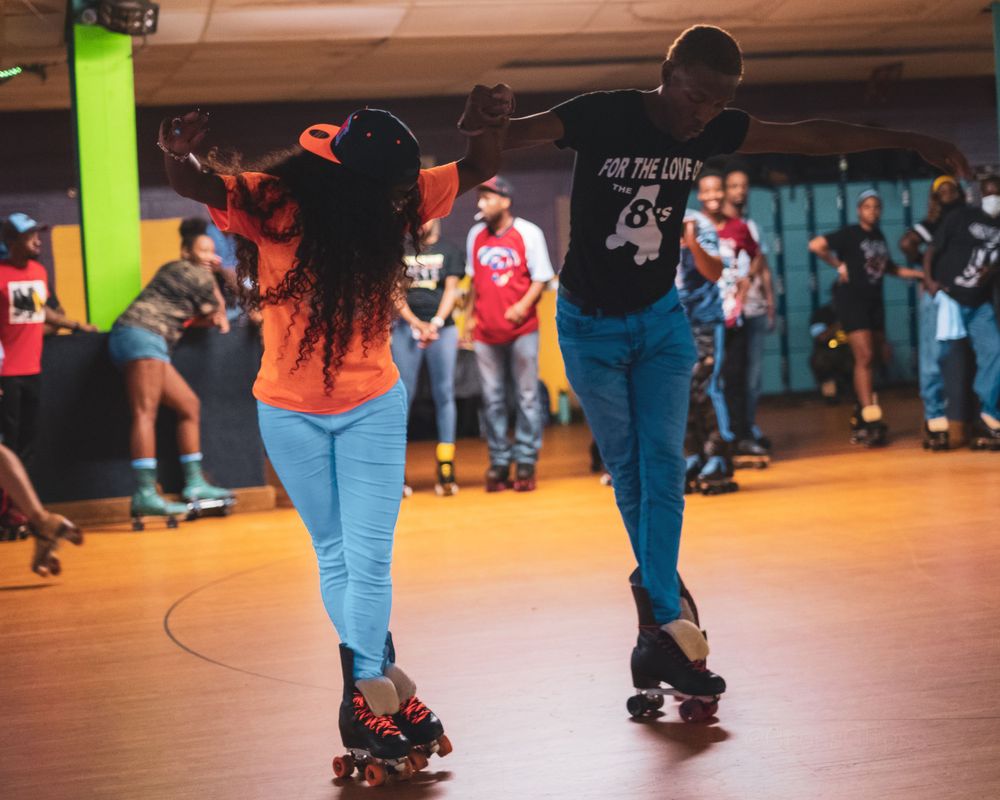 Two people roller skating together in a colorful indoor rink with crowd in background.