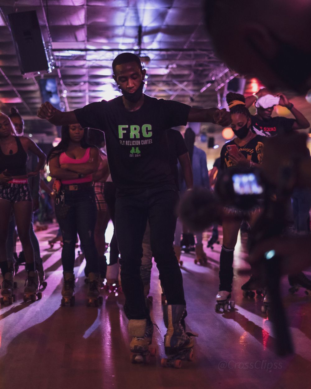 Roller skater in FRC shirt strikes pose under purple lighting at indoor skating venue.