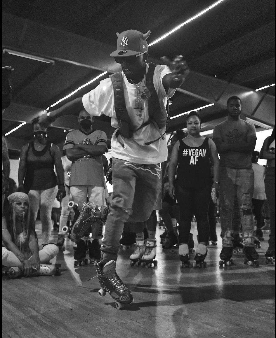 Roller skater in Yankees cap and white tank top performs at indoor skating event.