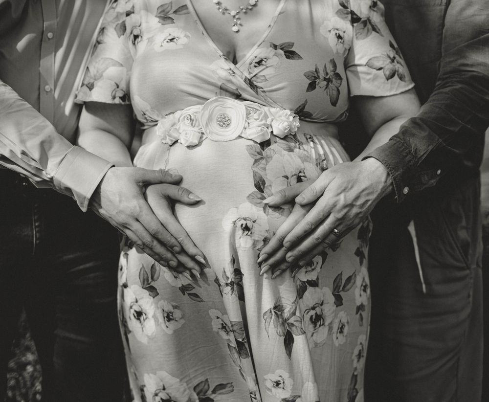 Black and white close-up of hands cradling pregnant belly in floral maternity dress.