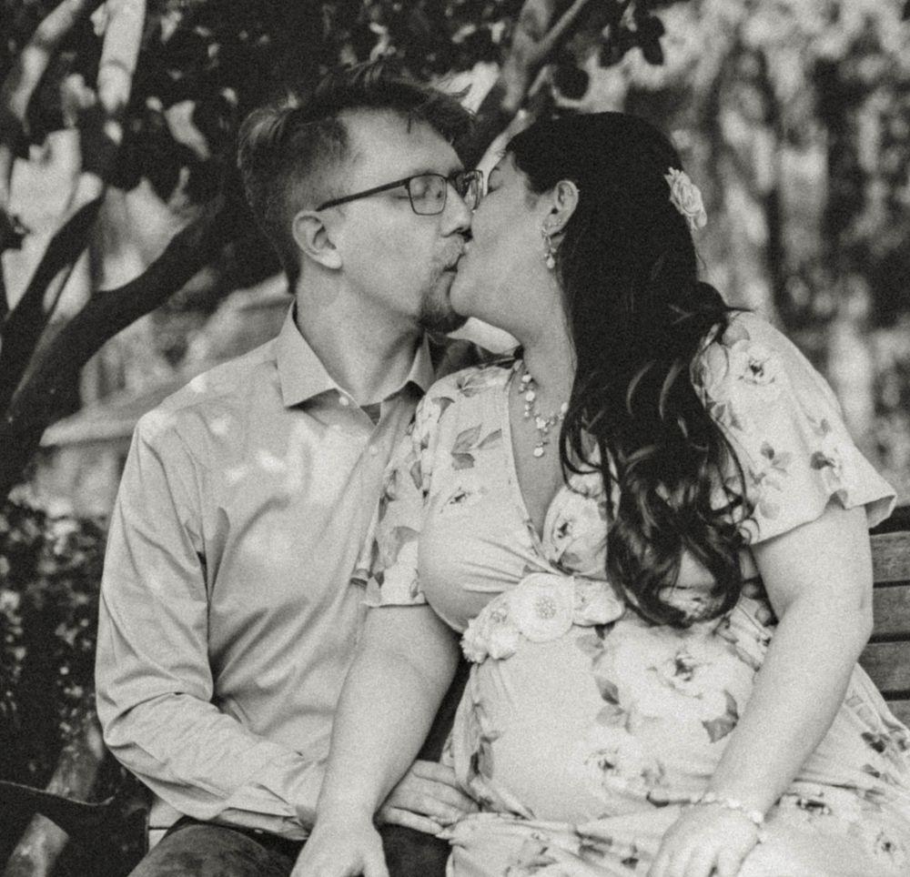 Black and white photo of a couple sharing a kiss outdoors during a maternity photo session.