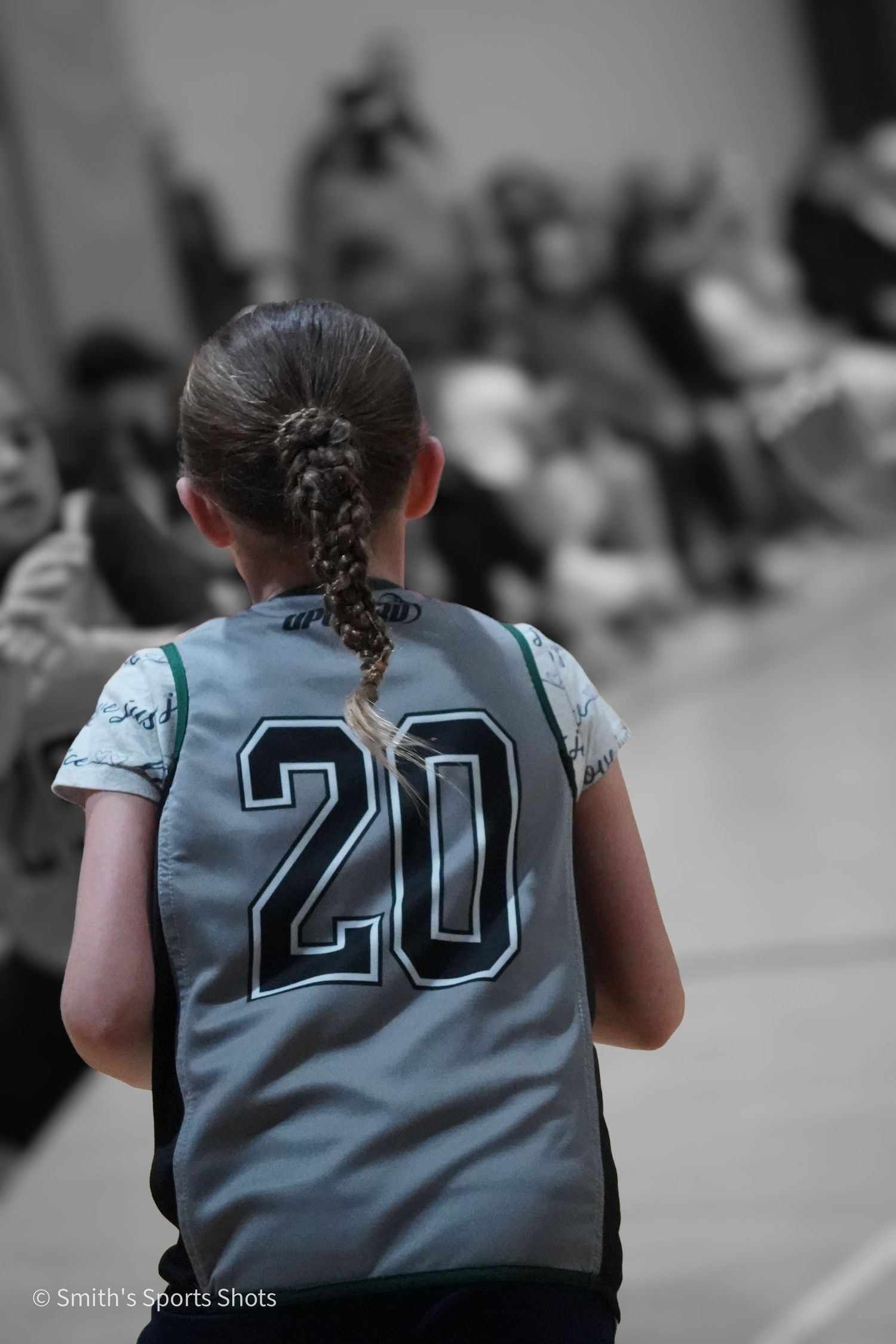 Youth athlete with braided hair wearing jersey number 20 shown from behind in a selective color sports photo.