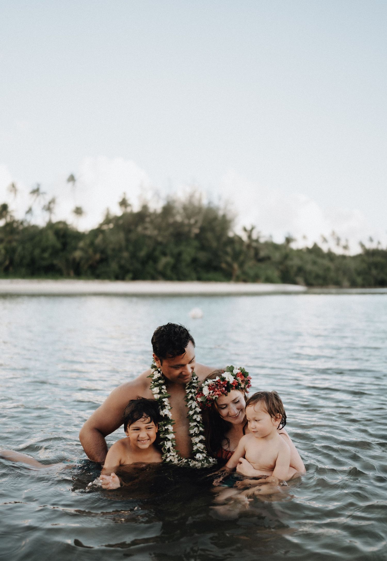 A family enjoying time together in tropical waters with palm trees along the shoreline in Hawaii.