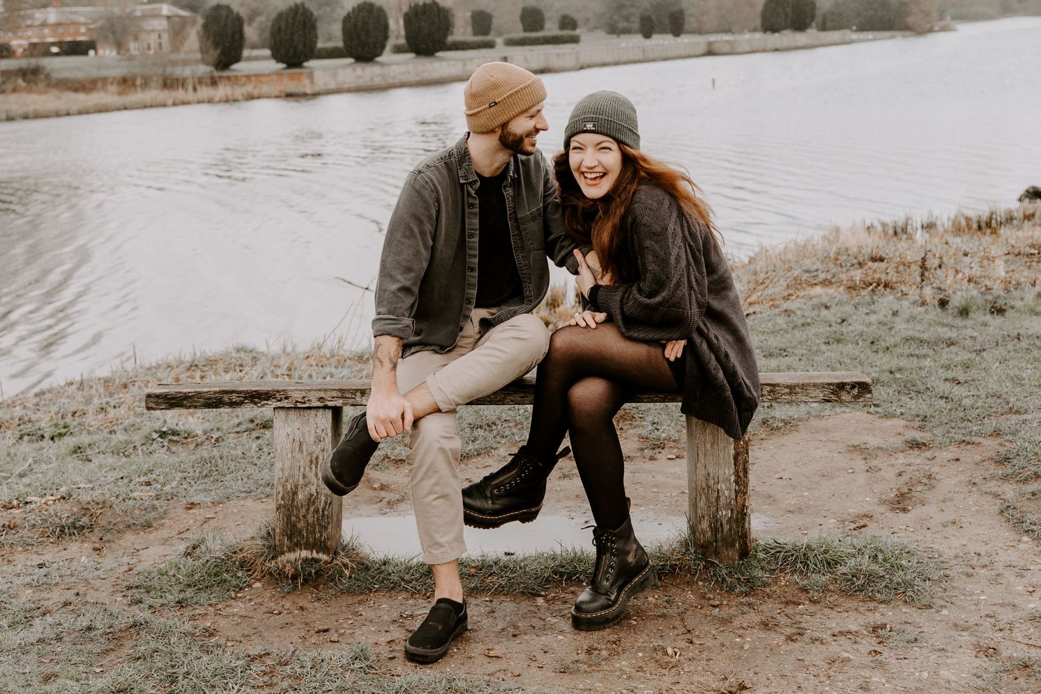 A couple are sat on a bench in front of a lake in Clumber Park in Lincolnshire. The lady is laughing towards the camera.