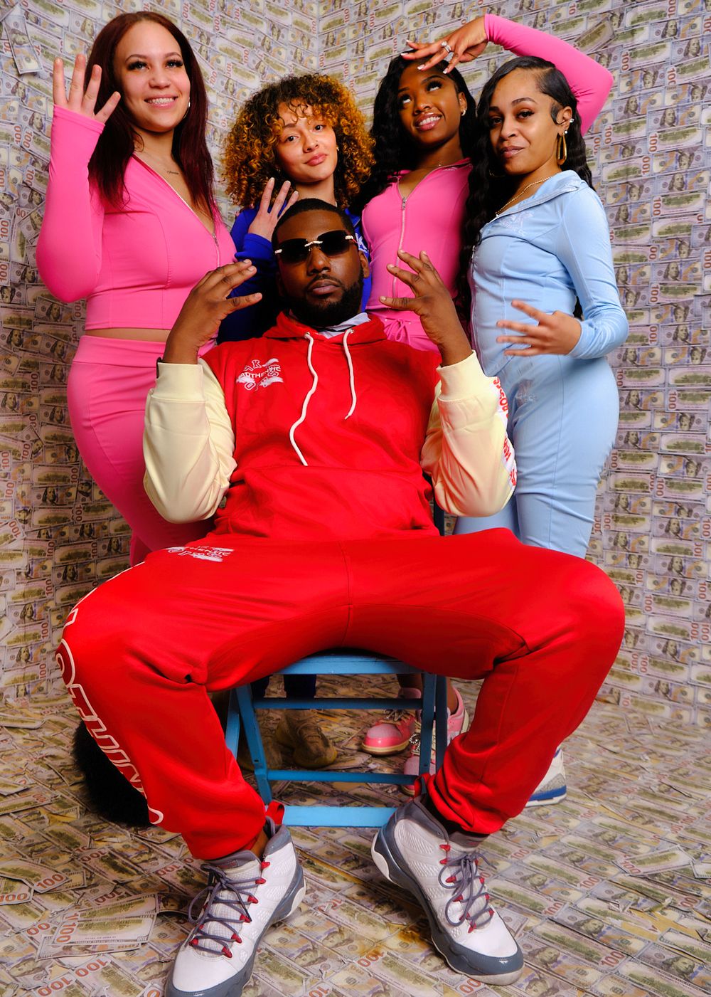 Group photo against money-print backdrop featuring people in colorful fitted outfits.