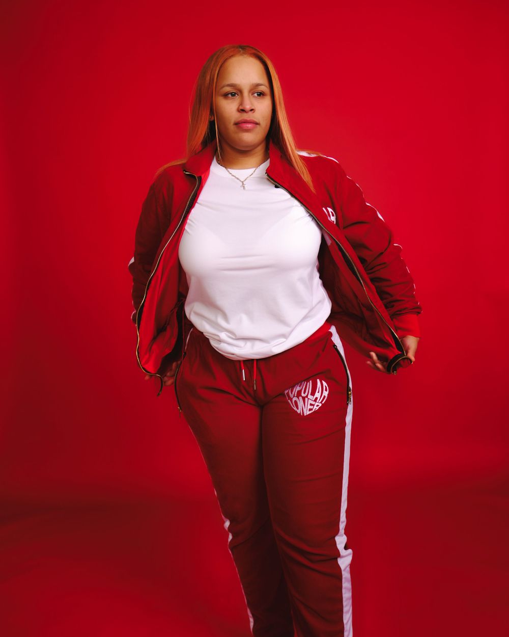 Athletic wear fashion photo featuring a red tracksuit and white t-shirt against a bright red background.