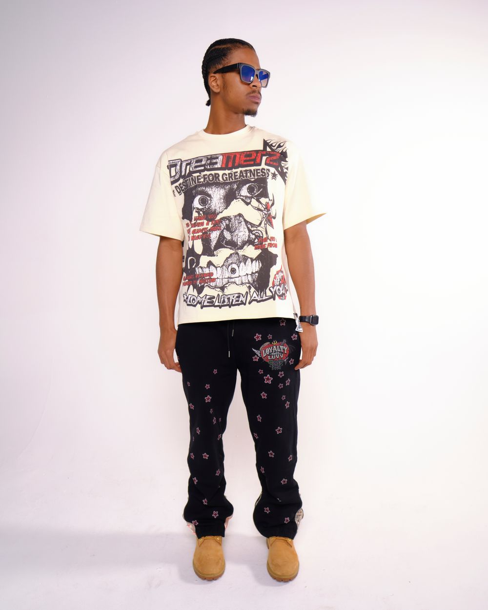 Model wearing vintage graphic t-shirt and printed pants with sunglasses strikes casual pose.