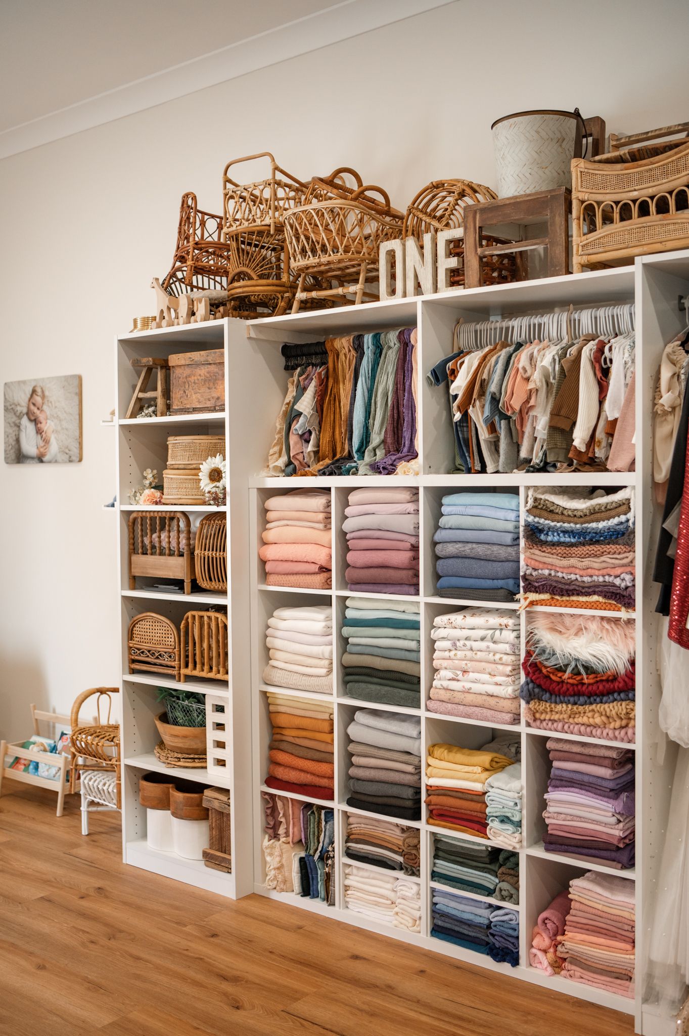 Organized white shelving unit displaying neatly folded textiles and linens in various colors with woven baskets on top.