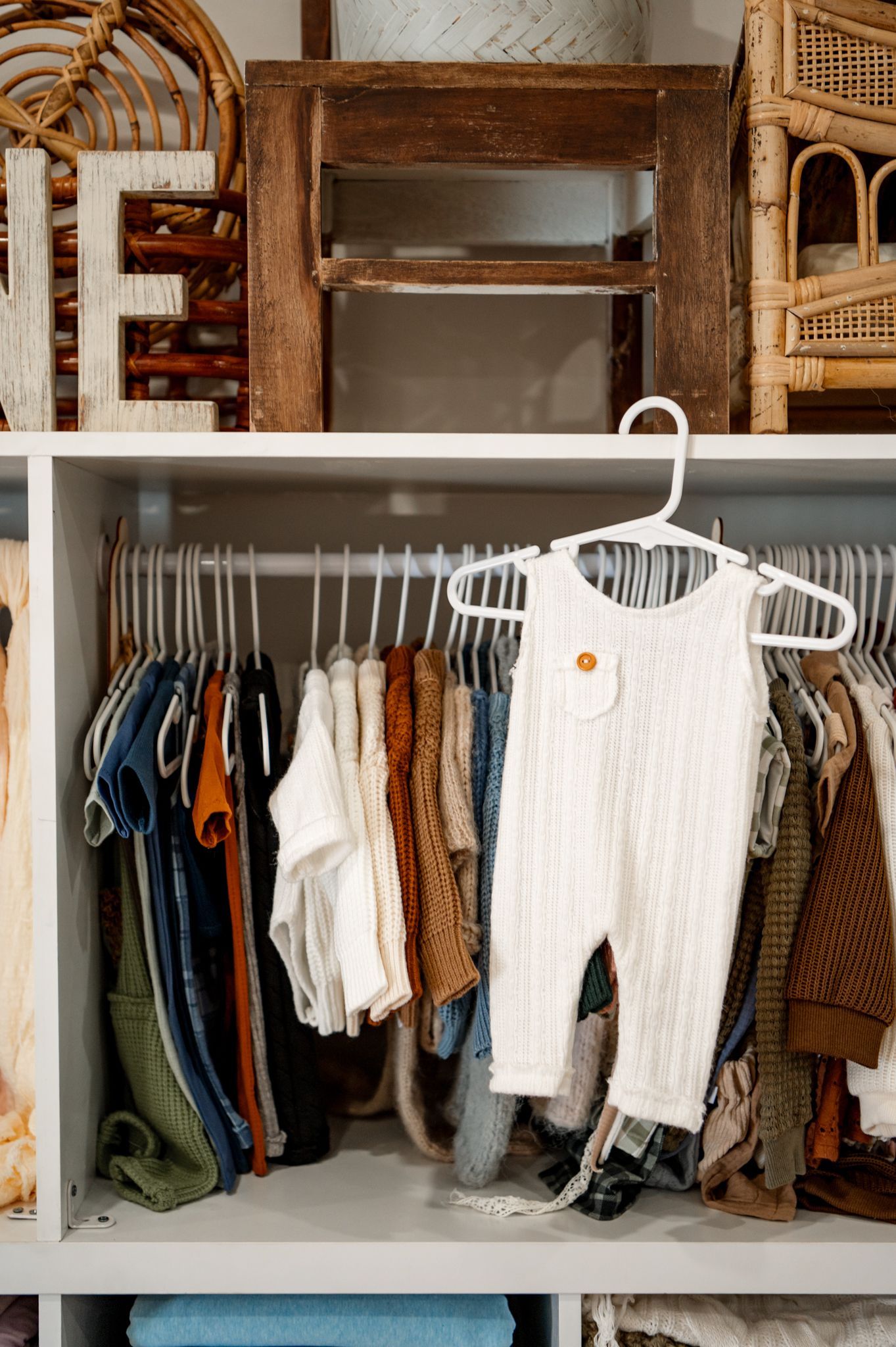 Organized closet with hanging clothes on white racks displaying a neutral color palette of casual and formal wear.