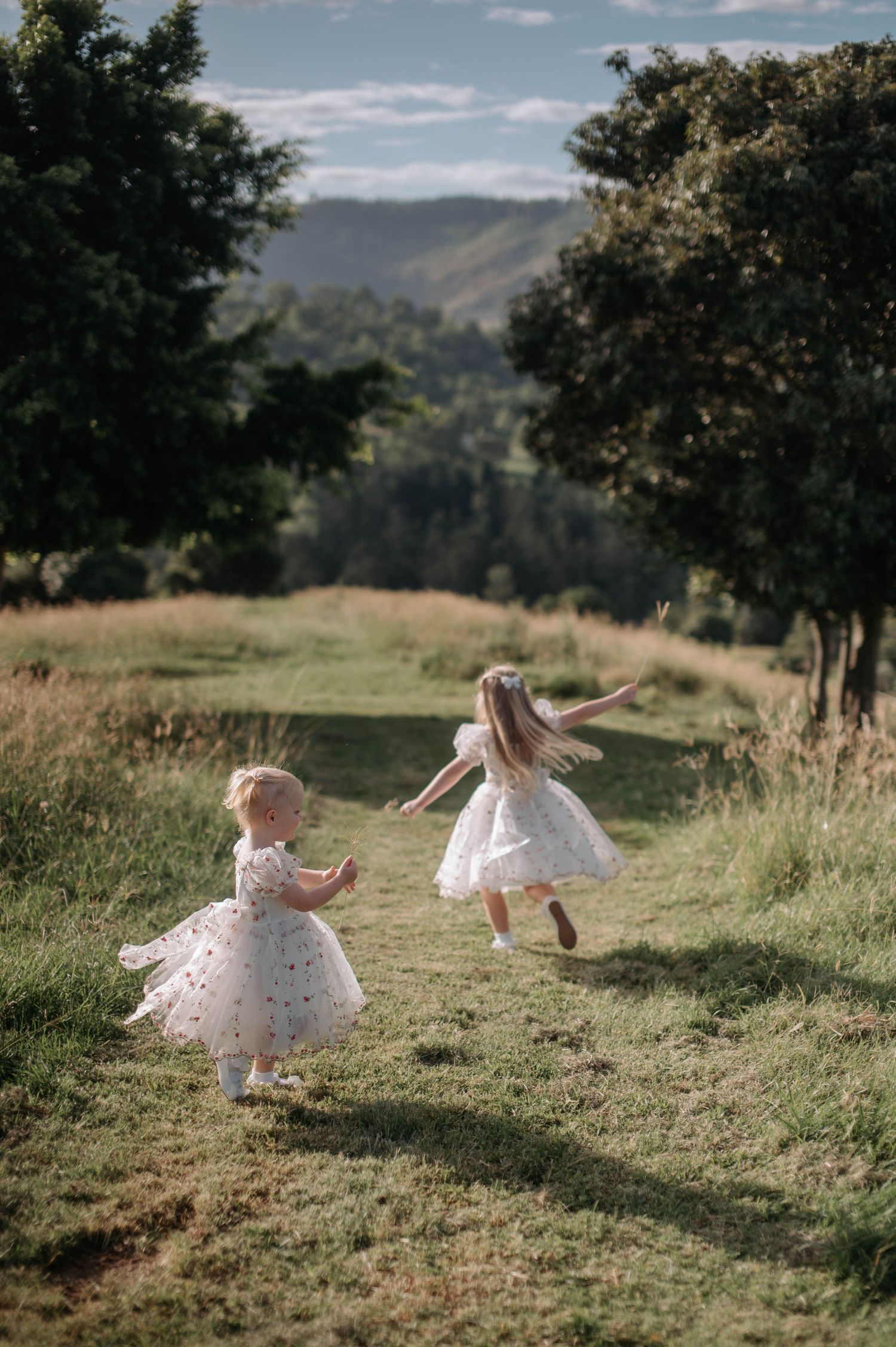 Children in white dresses dancing in field with mountains in background.