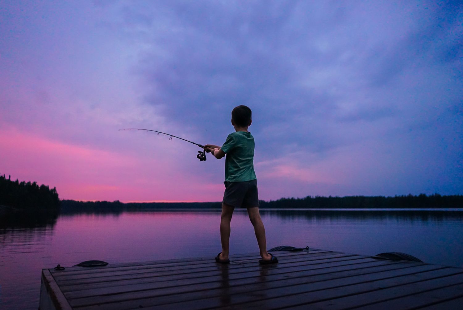 Fishing silhouettes against a vibrant purple sunset sky over a serene lake.