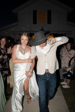 Couple celebrating at outdoor evening wedding reception with white bridal gown and beige suit walking together.