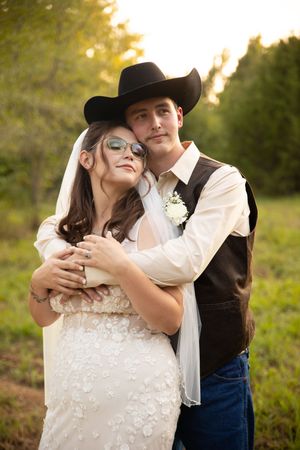 A romantic western-themed couple embraces in a sunlit field during their engagement photo session.