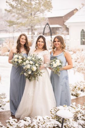 Bridesmaids in pale blue dresses pose with bride in white gown against snowy winter backdrop.