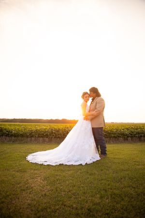 A couple embraces in a romantic sunset moment against a golden field backdrop during their wedding photoshoot.