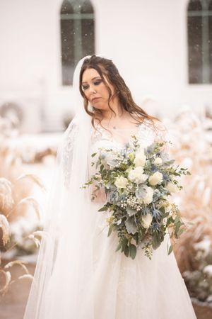 Bridal portrait with elegant white bouquet featuring roses and greenery against snowy background.