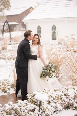 Romantic winter wedding portrait beside a white chapel in the snow.