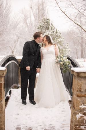 Newlyweds share a romantic moment on a snow-covered bridge.
