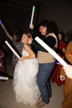Wedding reception guests dance and wave glow sticks in a darkened indoor venue.