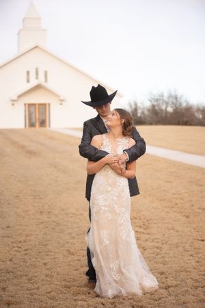 A romantic embrace between newlyweds outside a white country church.