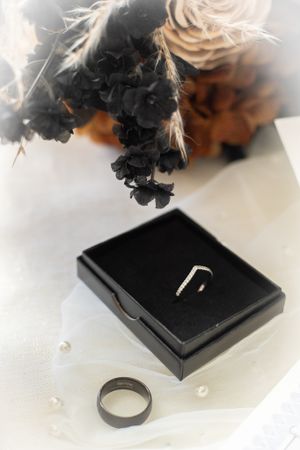 Wedding rings and black box with dried flowers on white surface in artistic composition.