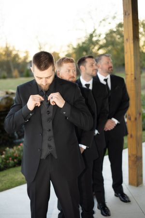 Groomsmen in black suits getting ready before outdoor wedding ceremony.