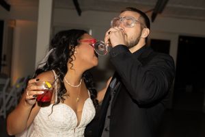 Wedding couple shares drinks and laughter during reception celebration.