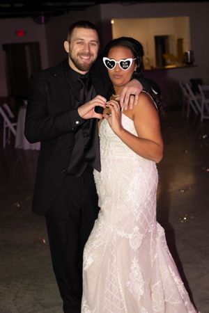 Couple in formal wedding attire poses playfully with novelty sunglasses.