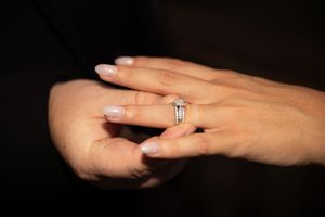 Close up of hands showing off engagement ring with diamond solitaire in multiple poses against dark background.