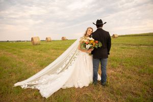 A romantic country wedding scene with a couple in a field of hay bales at sunset.