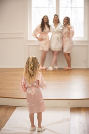 Little girl in pink robe watching wedding party members in matching robes.