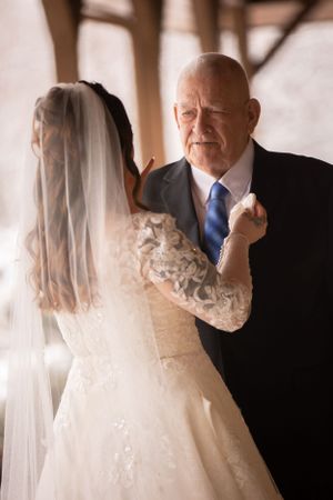 Tender moment between bride in lace dress and father before wedding ceremony.