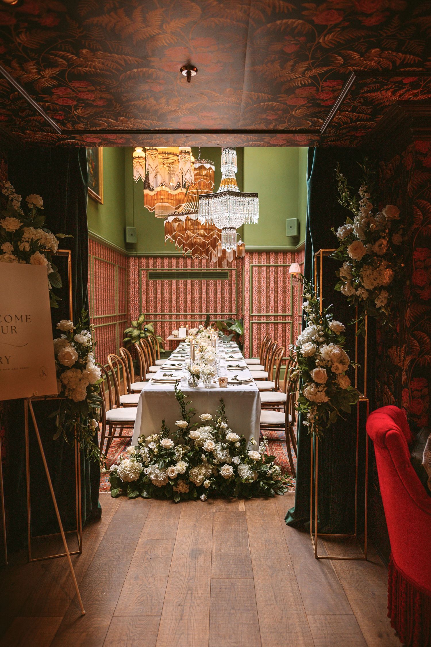 Elegant private dining room with crystal chandelier, pink walls, and white floral arrangements lining a long table setup.
