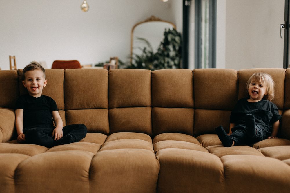 Two children laugh while sitting on a brown sectional couch in a modern living room.