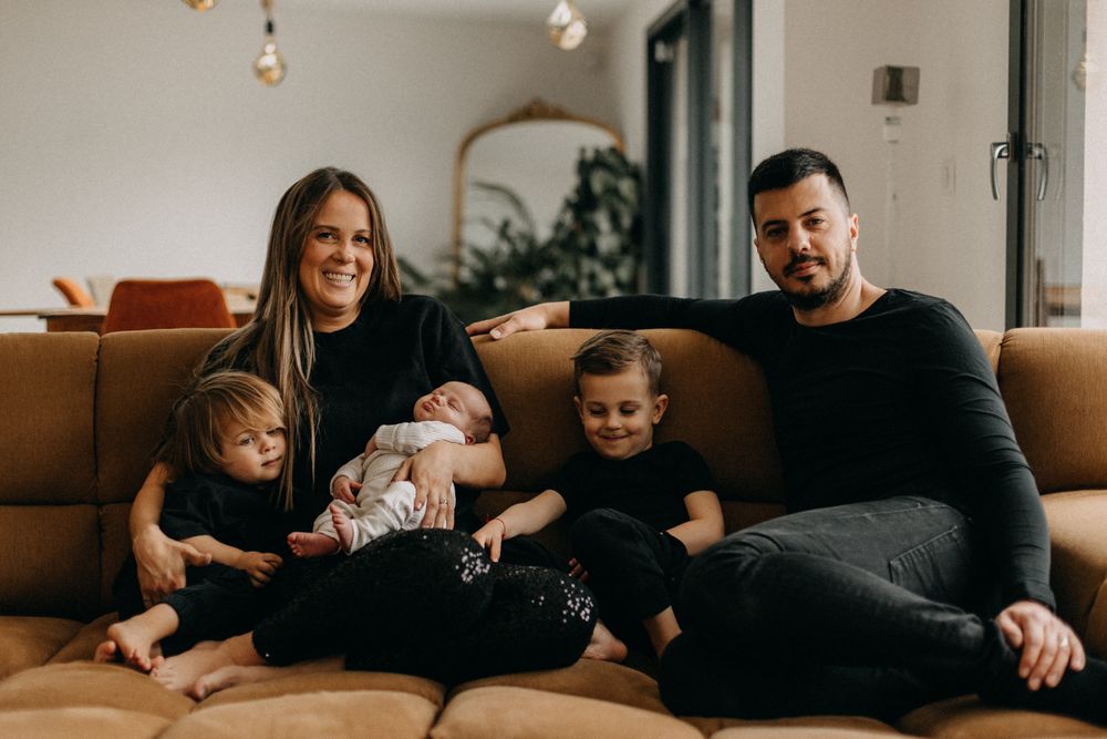Family of four relaxing together on tan sectional couch in living room.