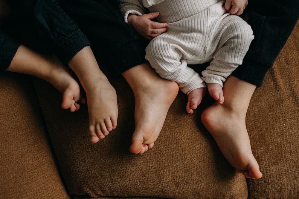 Bare feet of family members resting together on a brown couch in an intimate moment.