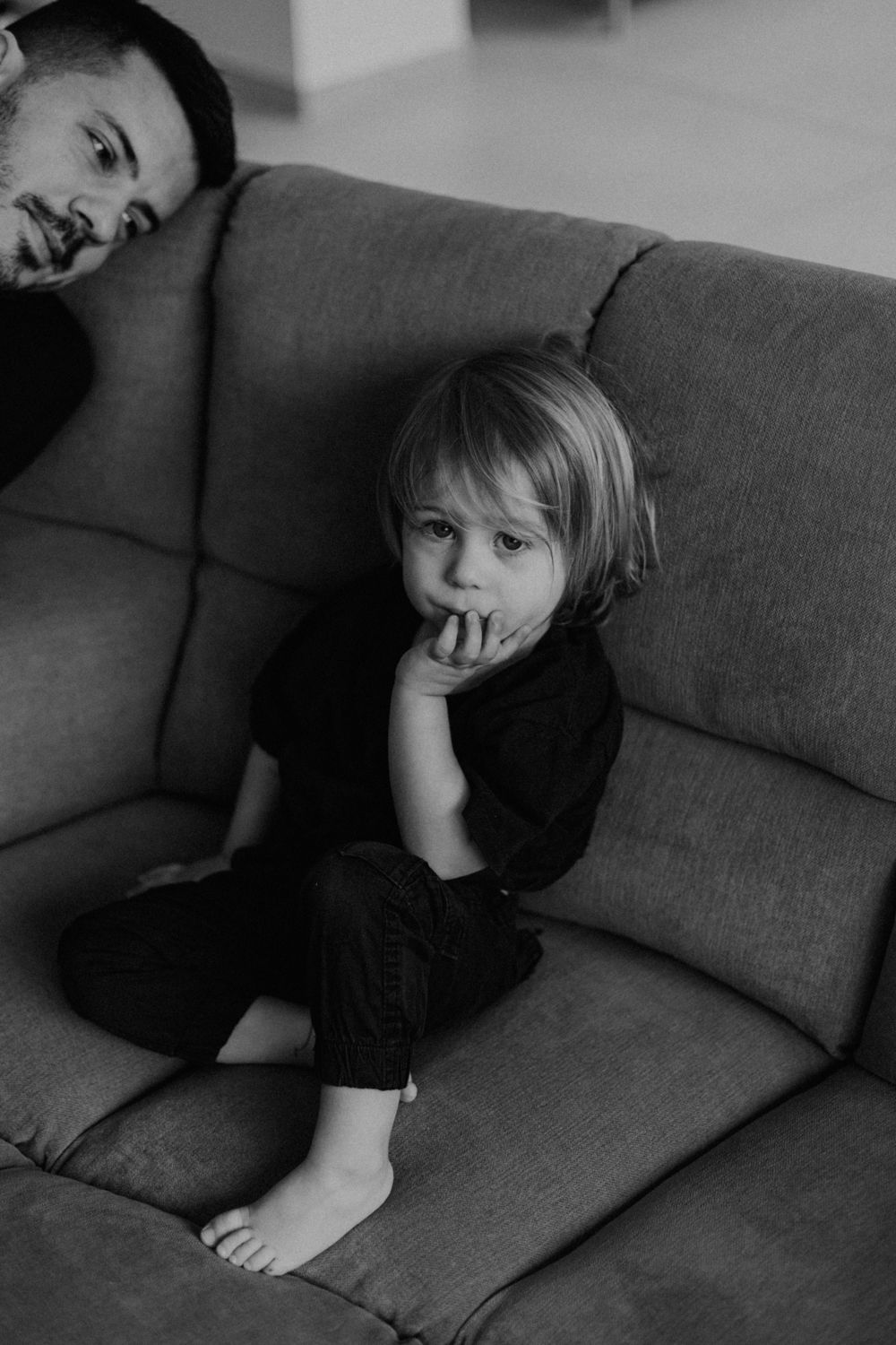 A black and white photo of two people relaxing on a gray couch.