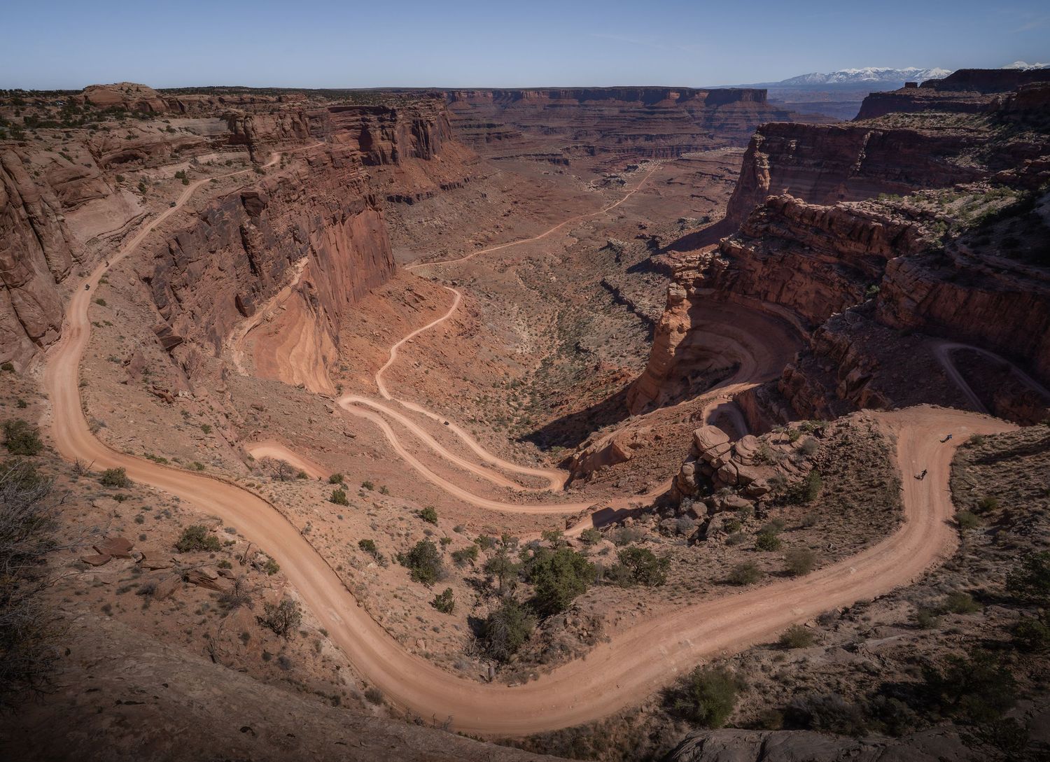 A long straight road leads towards snow-capped mountains under dramatic stormy clouds in a desert landscape.