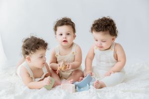 Three babies in matching sleeveless outfits interacting with toys on white backdrop.