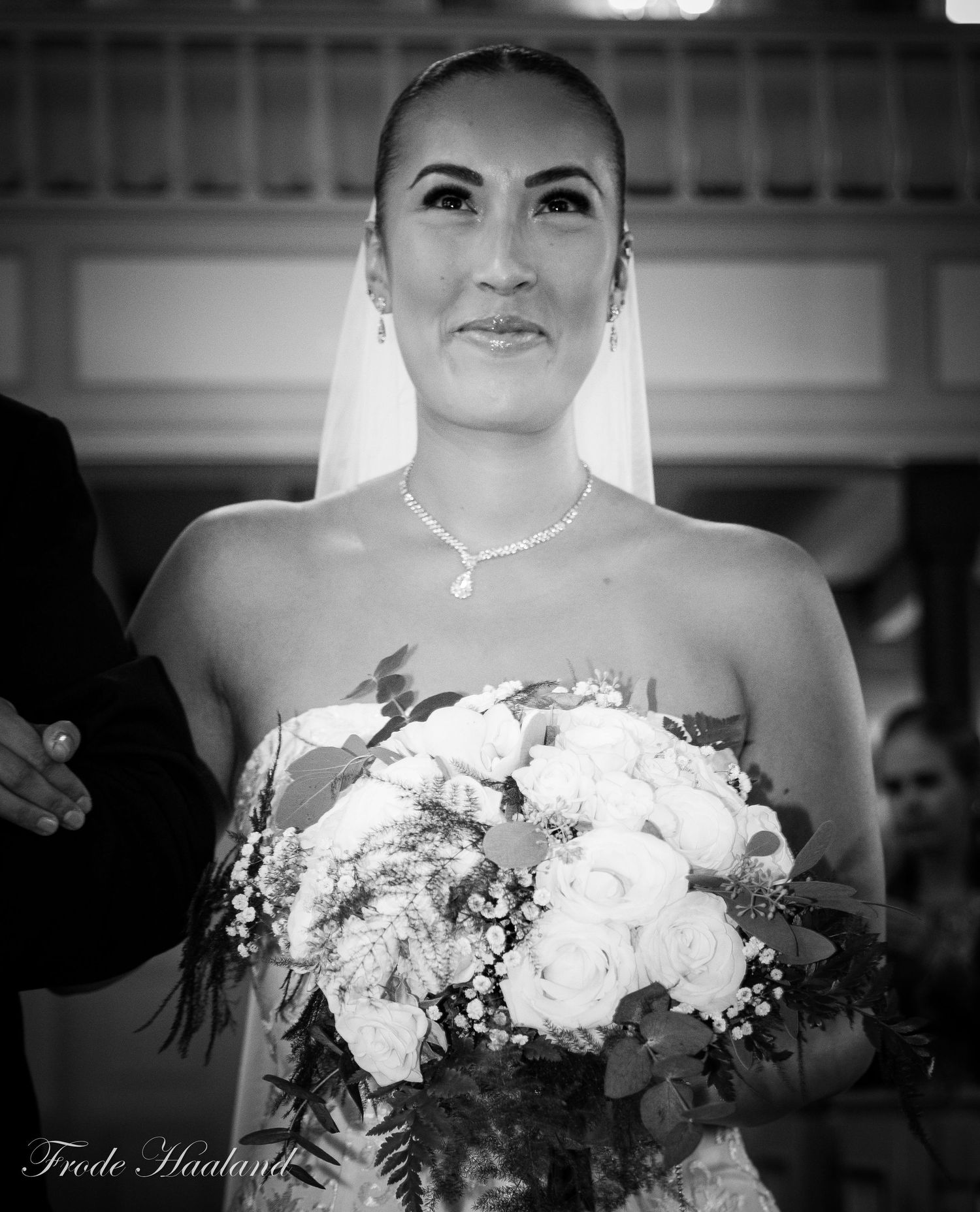 Elegant bride in a strapless gown holding white roses bouquet, smiling during wedding ceremony.