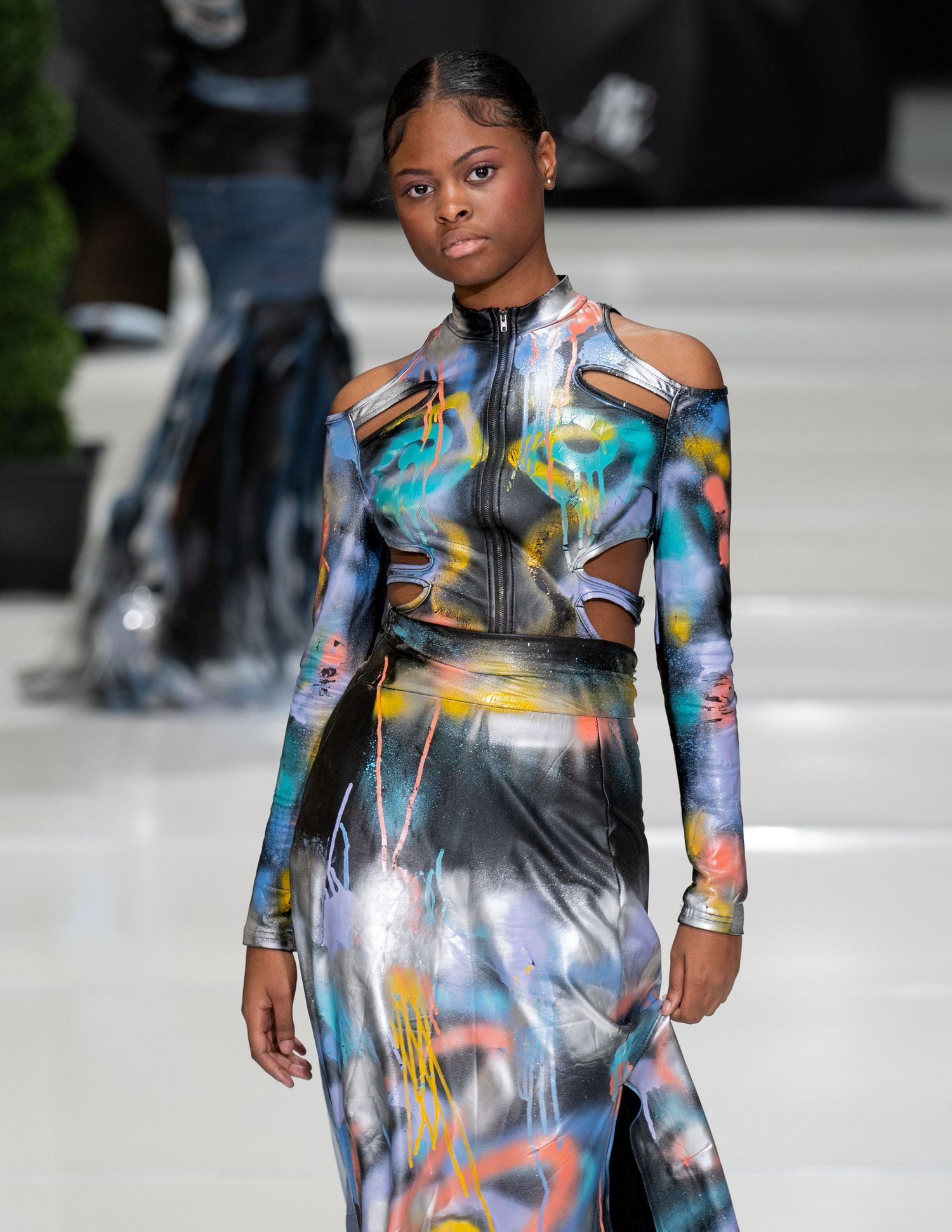 Futuristic holographic dress with cutout details and long sleeves on fashion runway.