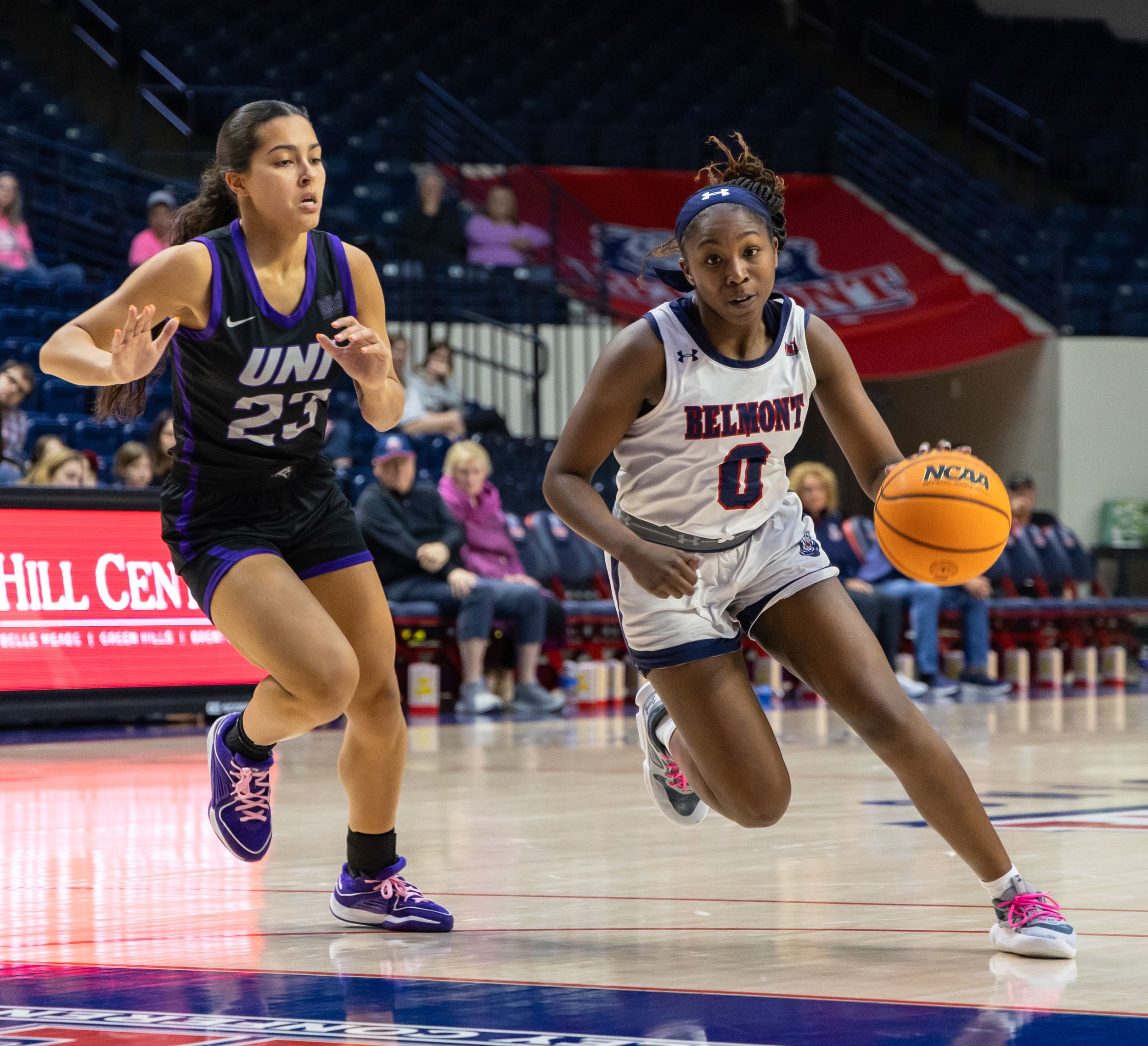 Belmont women's basketball player number 0 drives past UNI defender number 23 during college game.