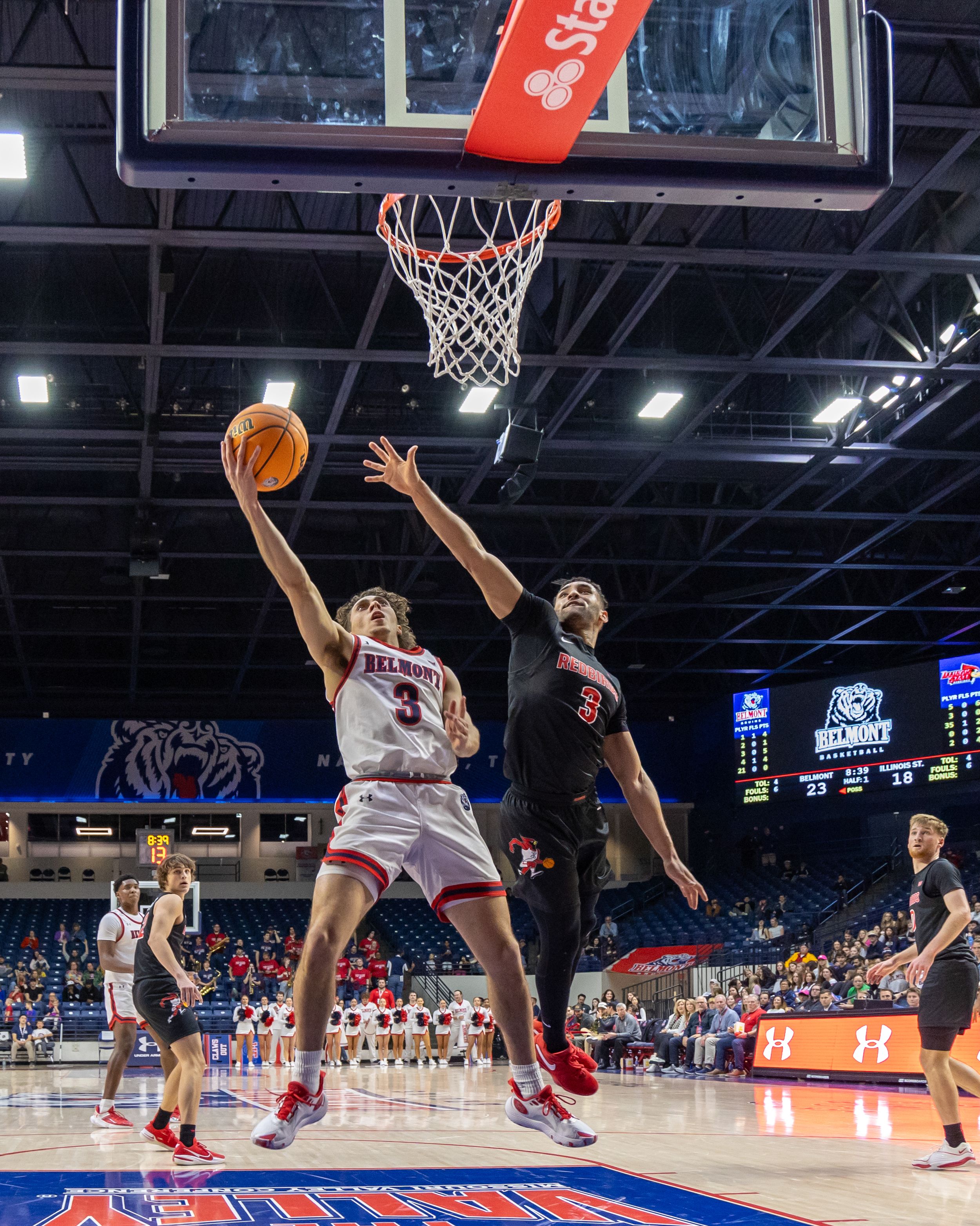 Belmont basketball player drives to the basket for a layup against a defender in college game.