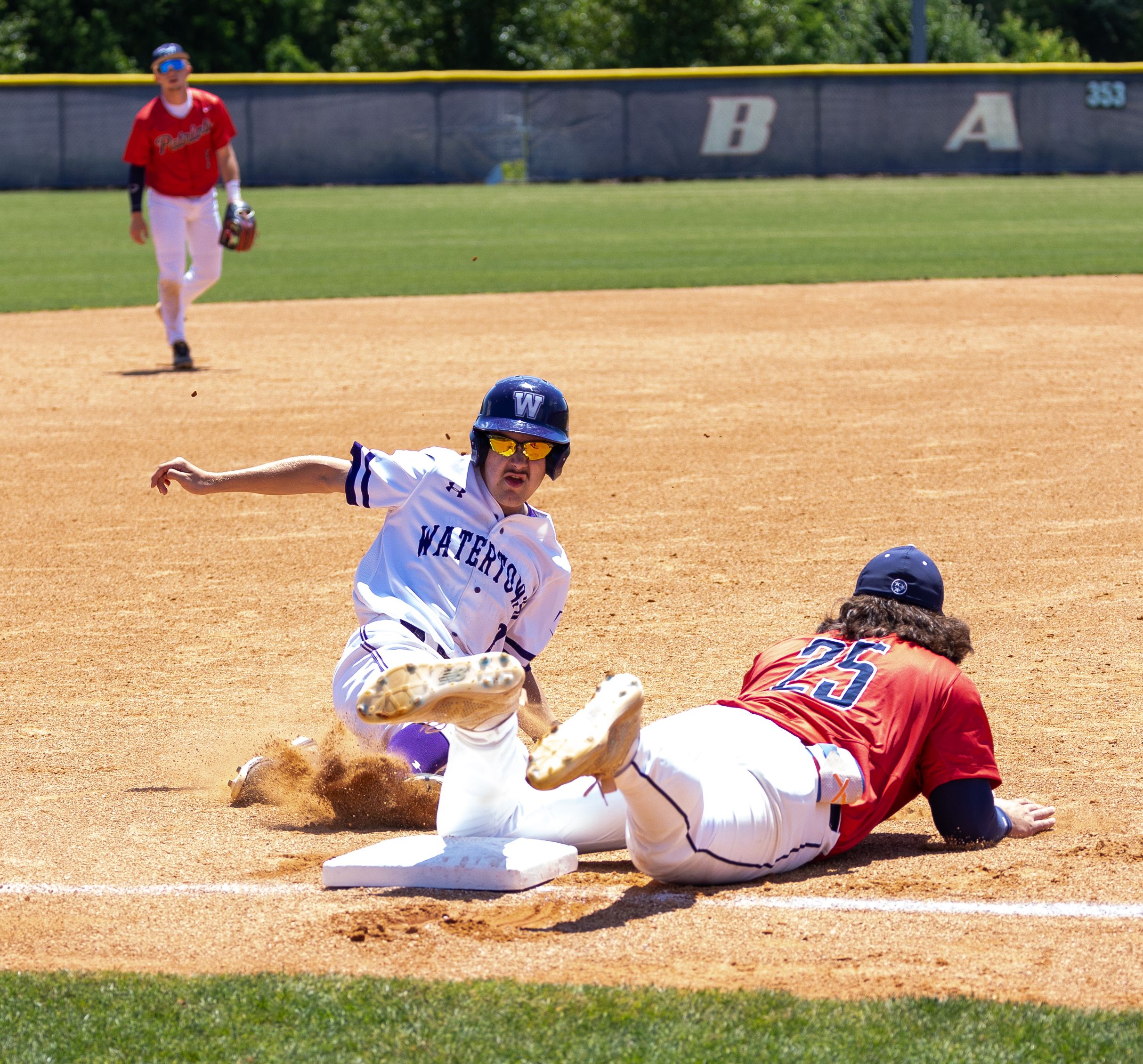 Baseball player slides into base as fielder attempts tag during competitive game.