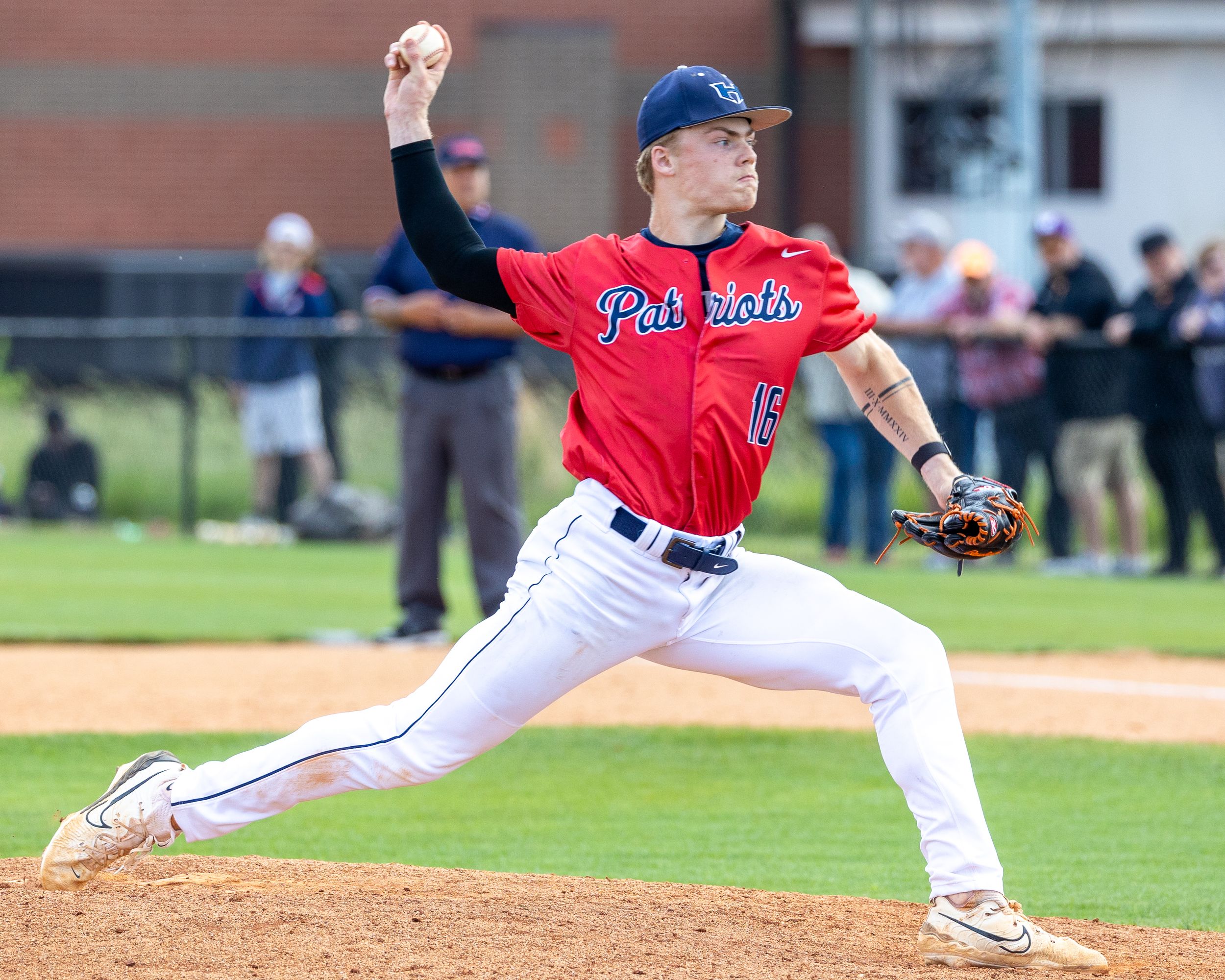 Patriots baseball pitcher delivers pitch during competitive game with crowd watching.