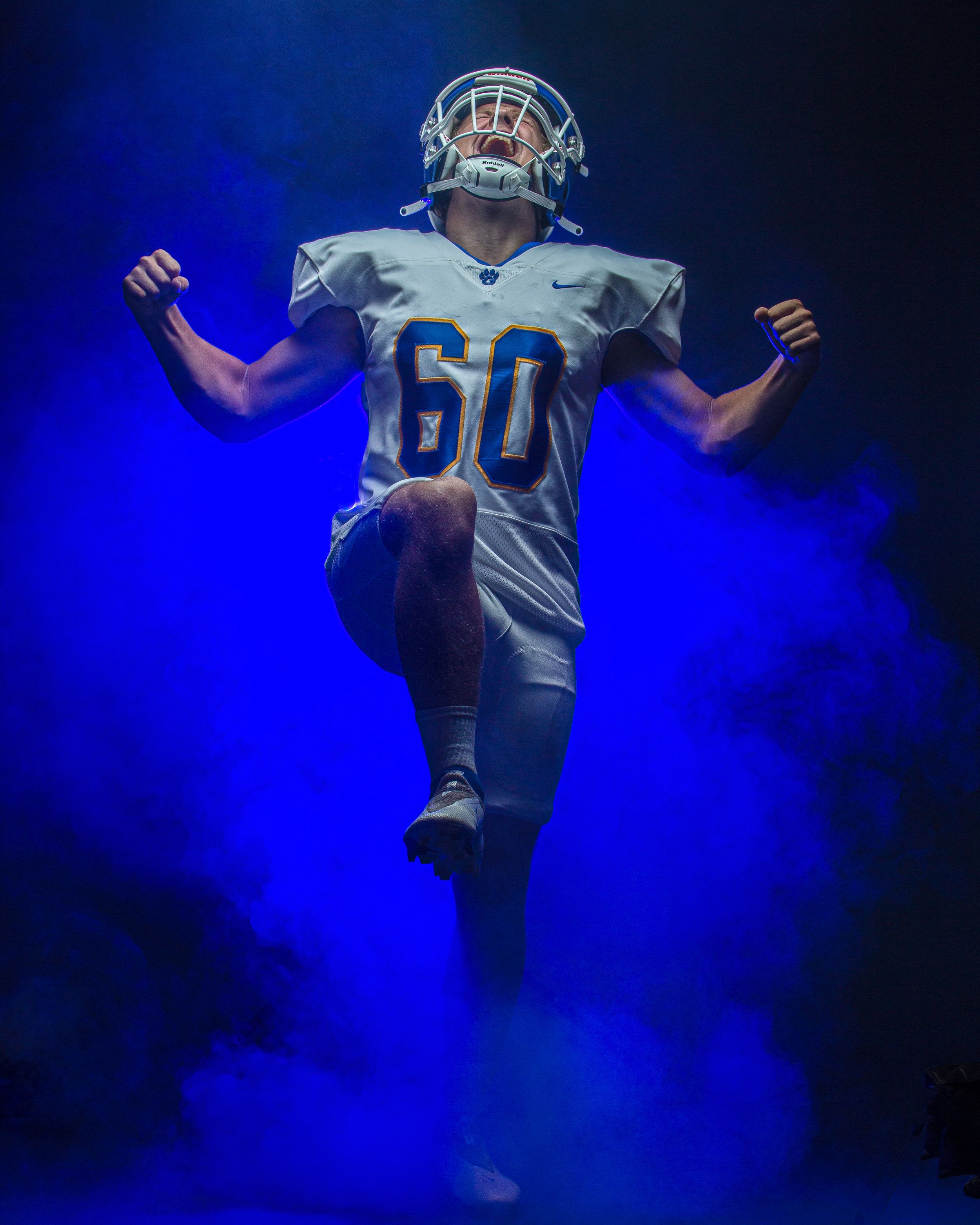 Football player wearing number 60 white uniform poses dramatically in blue smoke during a pregame entrance.